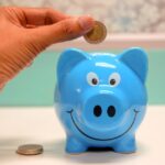 Hand inserting a coin into a blue piggy bank for savings and money management.